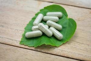 herbal medicine capsules with green herb leaf on wood table photo