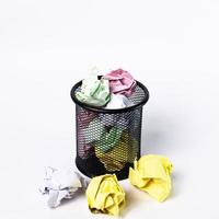 A small black basket made of round steel. Used to put garbage, documents that are not work and have been crushed so much that it overflows outside. In the white background there is copy space. photo