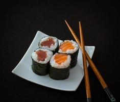 Four salmon, tuna maki sushi and black chopsticks on a black background