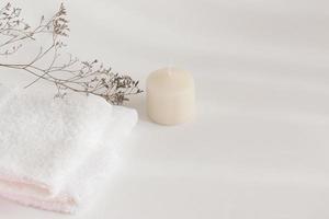 Towel, candle and dried wildflowers on a white table. Warm light and shadows photo