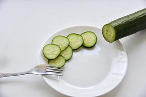 Whole and sliced cucumber on a white plate and fork photo