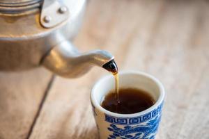 el té se vierte sobre el vaso de azulejos de la tetera. foto