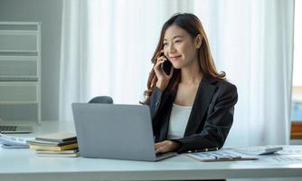 mujer de negocios asiática tiene la alegría de hablar por teléfono, computadora portátil y tableta en el escritorio de la oficina.