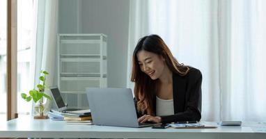 Charming asian businesswoman sitting working on laptop in office. photo
