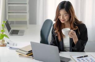 Smiling Asian businesswoman holding a coffee mug and laptop at the office. photo