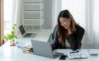 Happy young asian businesswoman sitting on her workplace in the office. Young woman working at laptop in the office. photo