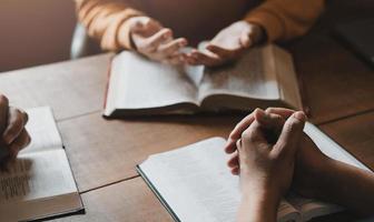 A group of Christians sit together and pray around a wooden table with blurred open Bible pages in their homeroom. Prayer for brothers, faith, hope, love, prayer meeting photo