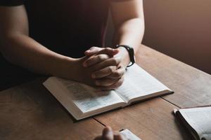 A group of Christians sit together and pray around a wooden table with blurred open Bible pages in their homeroom. Prayer for brothers, faith, hope, love, prayer meeting photo