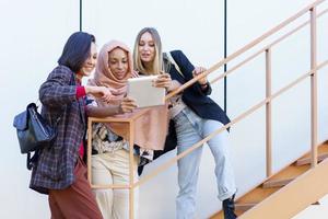 sonrientes jóvenes damas diversas usando tableta en las escaleras foto