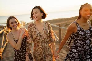 Content multiethnic girlfriends walking on footbridge on seashore photo