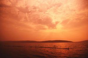 nubes de cielo rojo en el mar con fondo de isla de montaña en el océano, puesta de sol tropical en la playa foto