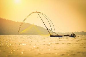 red de pescadores de asia usando en un barco de madera puesta de sol o amanecer en el río - barco de pescadores de silueta con fondo de isla de montaña en el océano foto