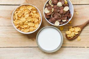 copos de maíz para el desayuno y varios cereales en tazón y taza de leche sobre fondo de madera para alimentos saludables de cereales