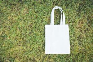 White tote canvas fabric eco bag cloth shopping sack on green grass background Zero waste Use less plastic say no plastic bag pollution problem photo