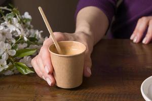 Coffee in a cardboard takeaway cup with a stirrer in a female hand on a table with flowers photo