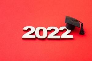 sombrero o gorra graduados con el número de madera 2022 sobre un fondo rojo. concepto de clase 2022 foto