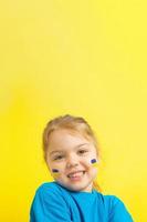 A girl with a painted Ukrainian flag of yellow and blue on her cheeks. Vertical photo with copy space