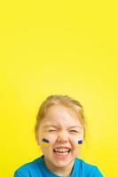 Smiling happy girl with a painted Ukrainian flag of yellow and blue on her cheeks. Vertical photo with copy space