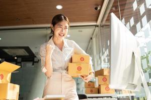 Portrait young attractive asia female owner startup business  work happy with box at home prepare parcel delivery in sme supply chain, procurement, omnichannel commerce online concept. photo