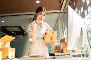 Portrait young attractive asia female owner startup business  work happy with box at home prepare parcel delivery in sme supply chain, procurement, omnichannel commerce online concept. photo