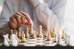 mano de hombre de negocios moviendo la figura del rey del ajedrez dorado y el oponente de jaque mate durante la competencia de tablero de ajedrez. concepto de estrategia, éxito, gestión, planificación empresarial, disrupción y liderazgo