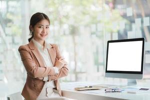 bella mujer asiática sonriente trabajando en la oficina, mirando la cámara. con pantalla en blanco de la computadora. foto