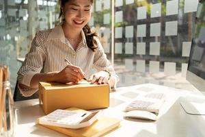 Starting small businesses SME owners female entrepreneurs Write the address on receipt box and check online orders to prepare to pack the boxes, sell to customers, sme business ideas online. photo