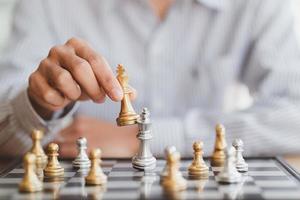 businessman hand moving gold Chess King figure and Checkmate opponent during chessboard competition. Strategy, Success, management, business planning, disruption and leadership concept photo