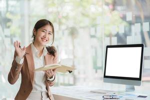 Beautiful smiling Asian woman working at the office, looking at the camera. with computer blank screen. photo