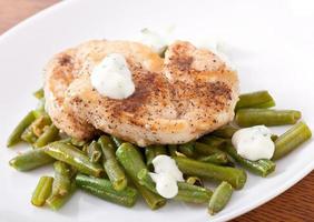 Grilled chicken breast with green beans and sauce on a white plate. photo