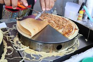 Hands are folding crispy crepe on hot plate. photo