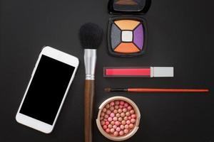 Cosmetic products and accessories on black background. Mobile phone with blank screen. Top view and copy space photo
