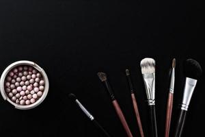 Makeup brush and cosmetics on black isolated background. Top view and mock up