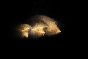 Golden sand explosion isolated on black background. Abstract sand cloud. Golden colored sand splash against dark background. Yellow sand fly wave in the air. photo