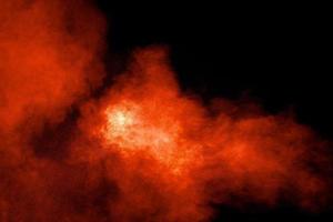 Abstract explosion of orange dust on black background.Freeze motion of orange powder burst. photo