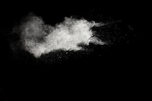 nubes de explosión de polvo blanco. movimiento congelado de partículas de polvo blanco salpicadas sobre fondo negro. foto