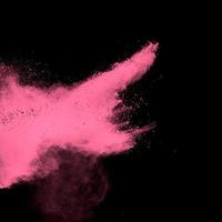 explosión de polvo rosa sobre fondo negro. nube de salpicaduras de polvo rosa sobre fondo oscuro. foto