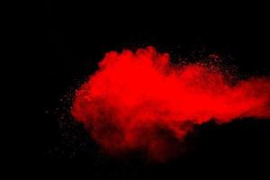 nube de explosión de polvo rojo sobre fondo negro. congelar el movimiento de salpicaduras de partículas de polvo de color rojo. foto