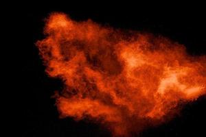 Abstract explosion of orange dust on black background.Freeze motion of orange powder burst. photo