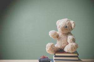 Vintage picture style. This cuddly fluffy doll is perfect for children. As a gift for children to play. A single brown teddy bear sitting on books old wooden table filling sad, alone with copy space. photo