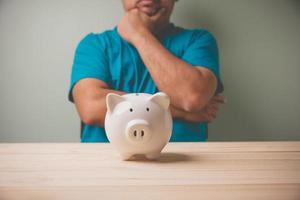 A white piggy bank on a wooden table with a man consider a white piggy bank to plan to save money for Investment future use. Concept saving, financial planning to the future, Business, Accounting.