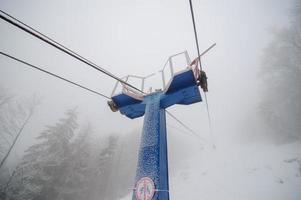 Cableway up to the mountain in the winter forest. The forest is covered with snow. Foggy weather. Bad visibility. photo