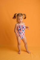 A little girl dressed in a swimsuit at the age of one and a half years is jumping or dancing. The girl is very happy. Picture taken in the studio on a yellow background. photo