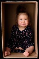 una niña linda y hermosa se sienta en una caja. foto