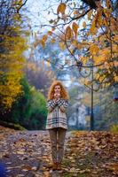 Beautiful red-haired girl with curly hair and blue eyes. The girl is wearing a checkered jacket. The girl is sitting on a bench. photo