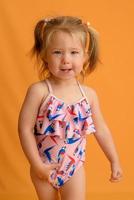 A little girl dressed in a swimsuit at the age of one and a half years is jumping or dancing. The girl is very happy. Picture taken in the studio on a yellow background. photo