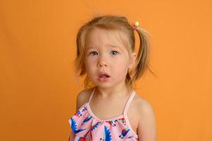 A little girl dressed in a swimsuit at the age of one and a half years is jumping or dancing. The girl is very happy. Picture taken in the studio on a yellow background. photo