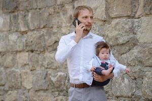 A young father is talking on a cell phone and holds his little daughter in his arms. copy space photo