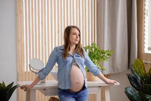 Pregnant woman stands near the table at her home photo