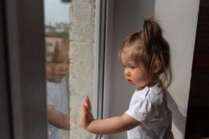 little girl looks out the window and asks outside during quarantine caused by coronavirus. photo